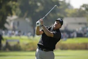 Male golfer swinging club on course.